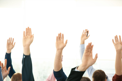 Photo of People raising hands to ask questions at business training on light background, closeup