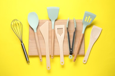 Photo of Different spatulas, whisk and tongs on yellow background, flat lay