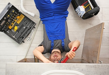 Photo of Professional plumber with set of tools working indoors, top view