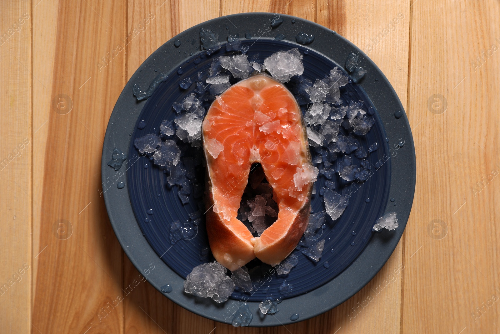 Photo of Fresh raw fish steak with ice on wooden table, top view