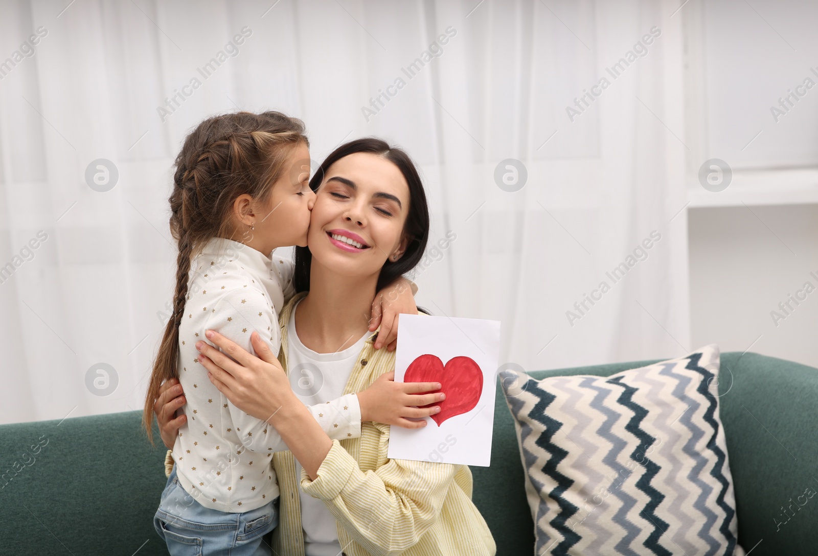 Photo of Happy woman with her daughter and handmade greeting card on sofa at home, space for text. Mother's day celebration