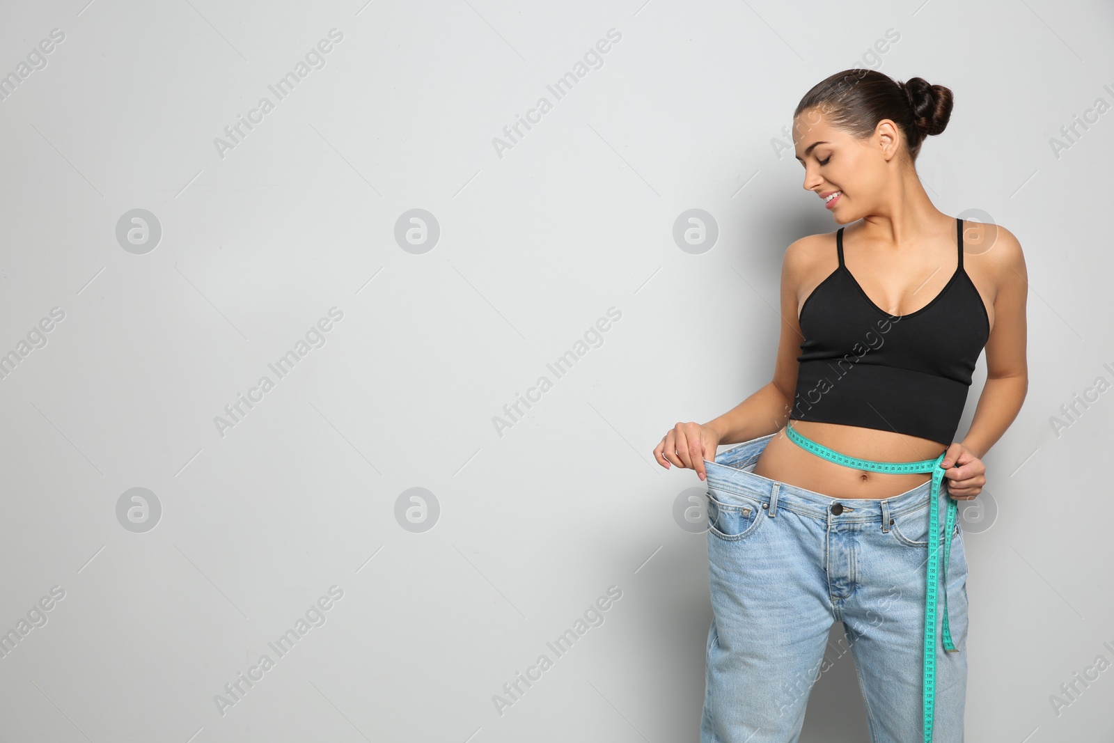 Photo of Slim woman in oversized jeans with measuring tape on light background, space for text. Weight loss