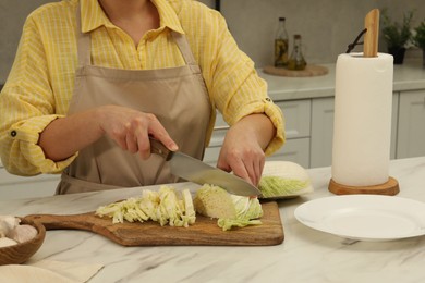 Photo of Woman cutting fresh chinese cabbage at table in kitchen, closeup