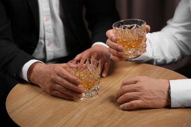 Men with glasses of whiskey at wooden table indoors, closeup