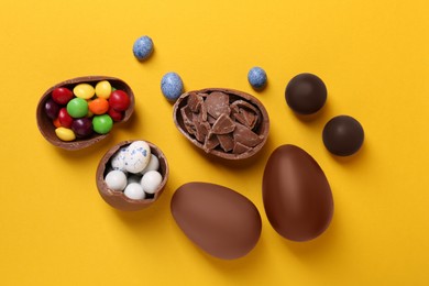 Photo of Whole and halves of chocolate eggs with colorful candies on yellow background, flat lay