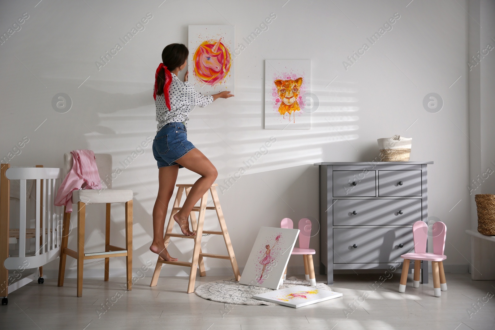 Photo of Decorator hanging picture on white wall in baby room. Interior design