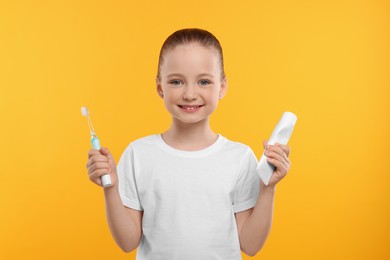 Photo of Happy girl holding electric toothbrush and tube of toothpaste on yellow background