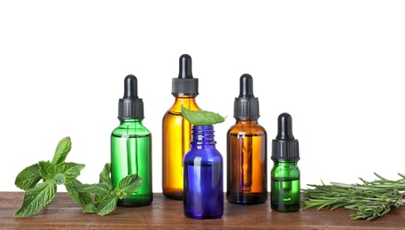 Bottles of herbal essential oils on wooden table against white background