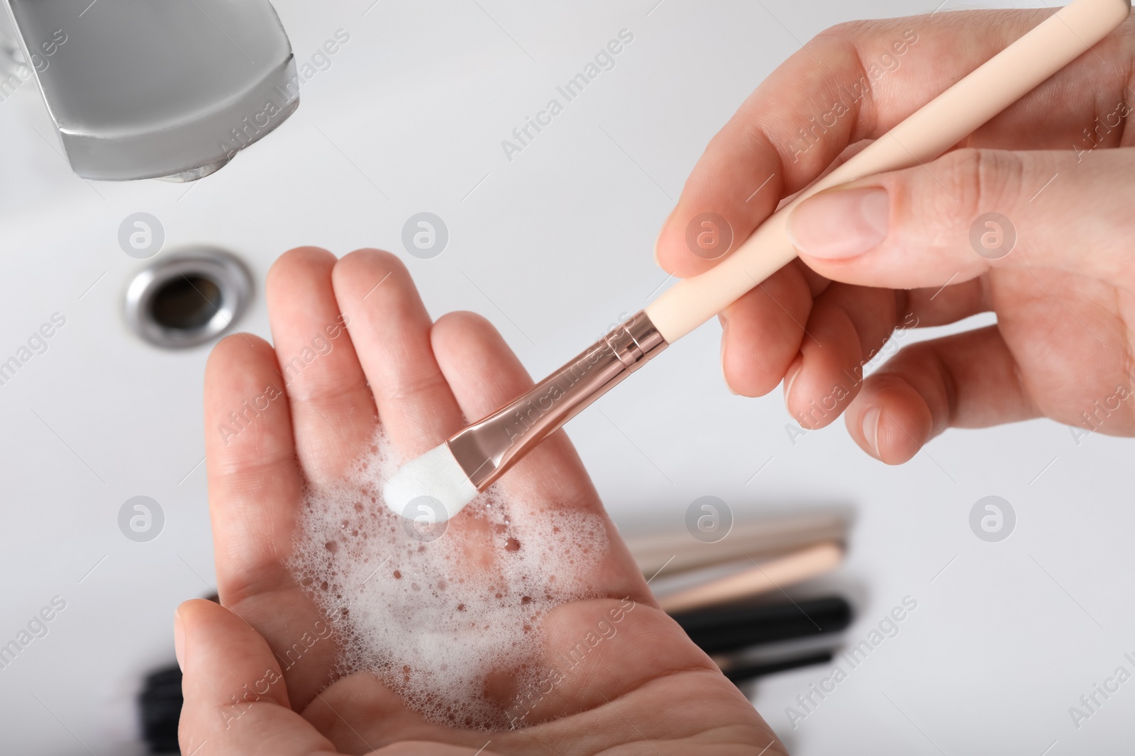 Photo of Woman washing makeup brush with soap, closeup