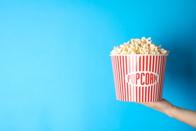 Photo of Woman holding popcorn bucket on color background, closeup with space for text. Cinema snack