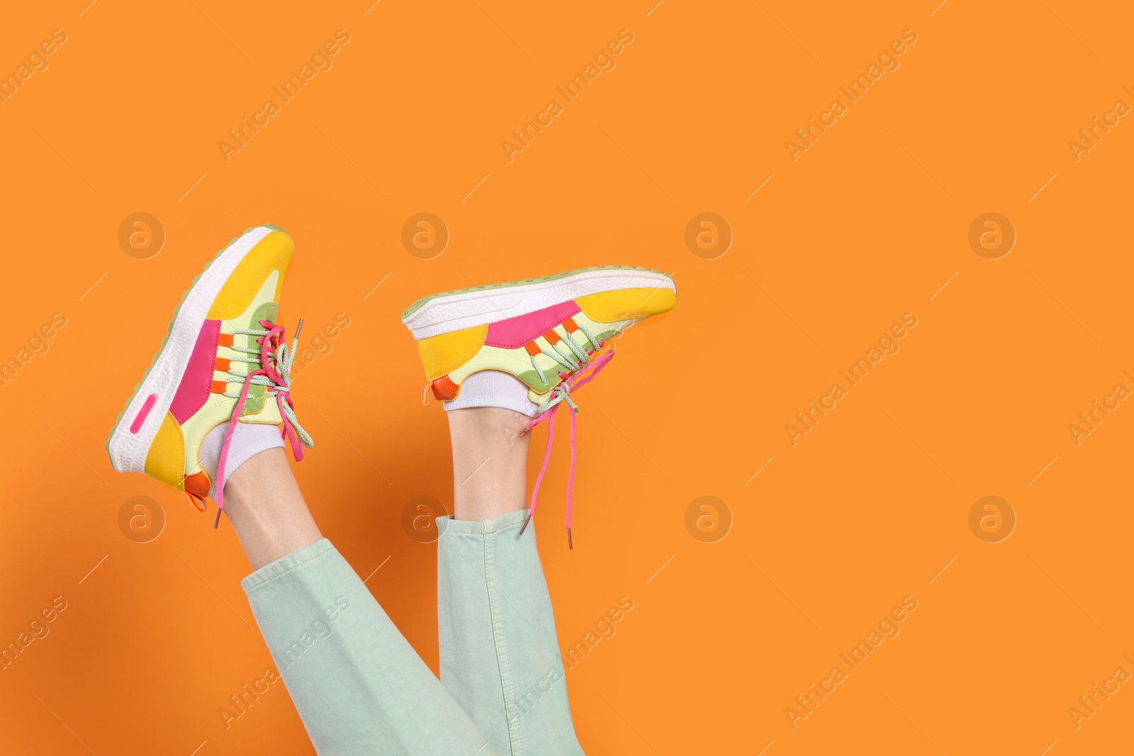 Photo of Woman wearing pair of new stylish sneakers on orange background, closeup. Space for text