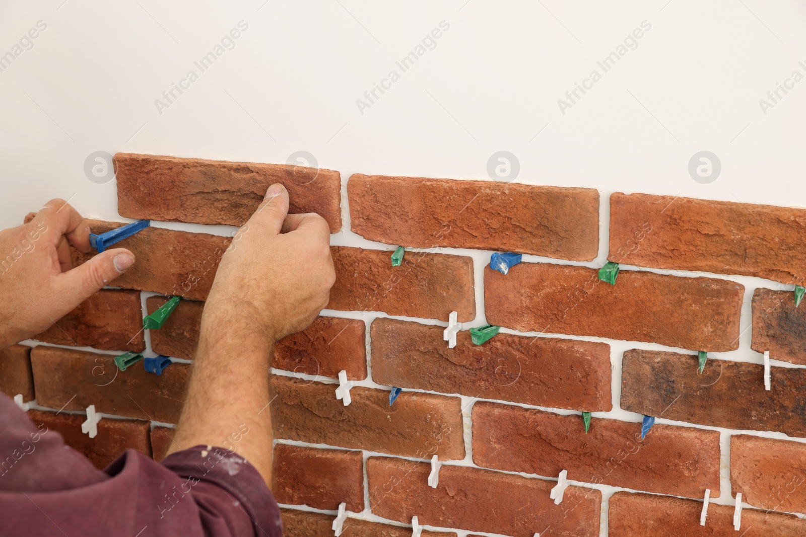 Photo of Professional builder installing new brown decorative bricks on wall, closeup