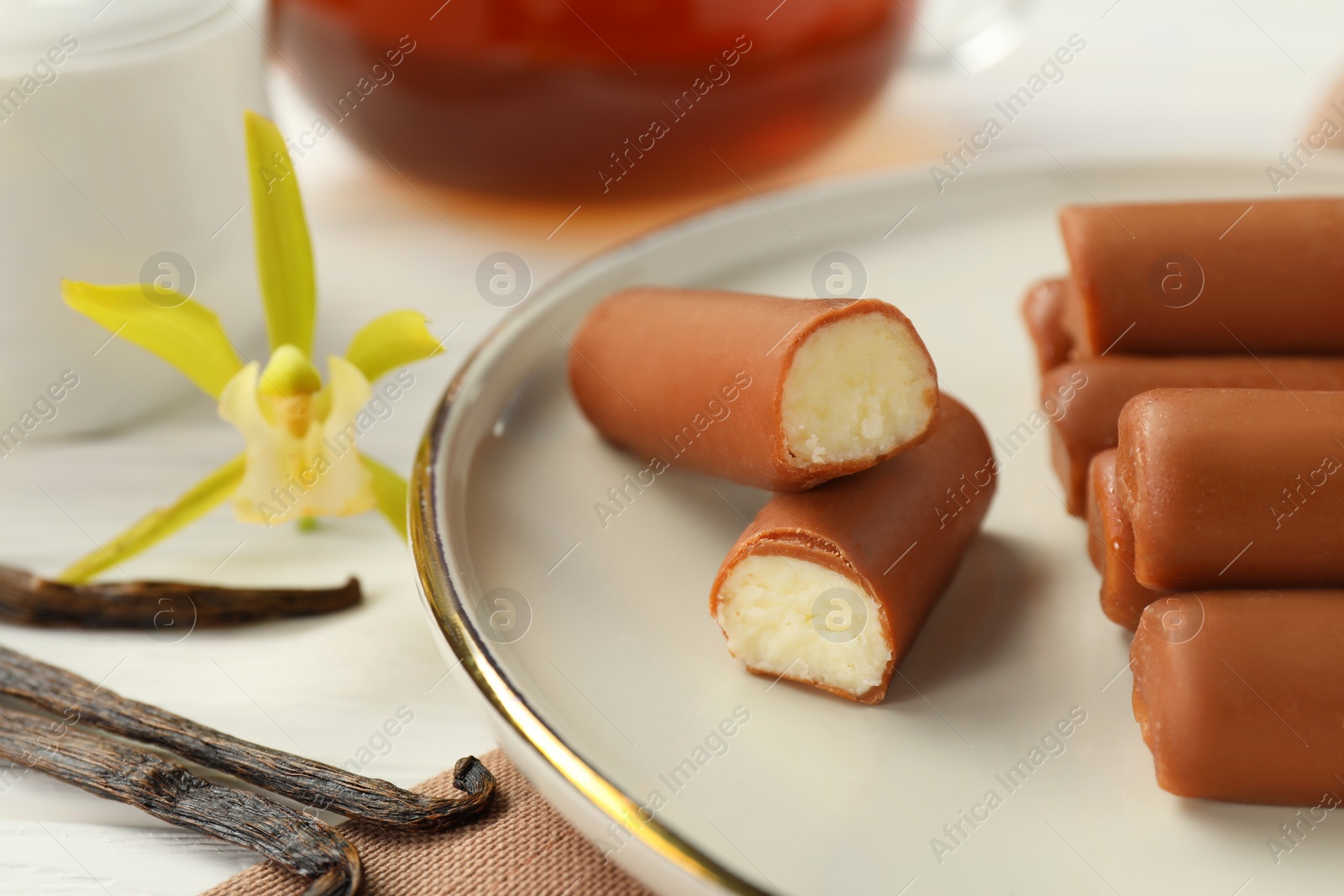 Photo of Glazed curd cheese bars, vanilla pods and flower on white wooden table, closeup