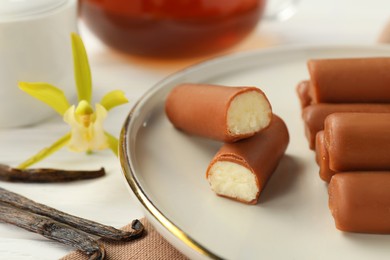 Glazed curd cheese bars, vanilla pods and flower on white wooden table, closeup