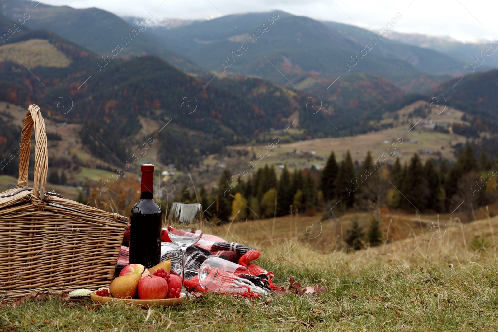 Photo of Wicker picnic basket, wine, snacks and plaid in mountains on autumn day, space for text