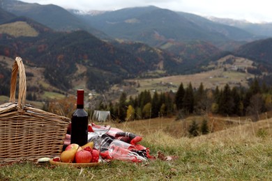 Photo of Wicker picnic basket, wine, snacks and plaid in mountains on autumn day, space for text