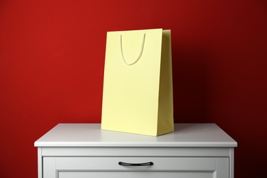 Photo of Paper shopping bag on white chest of drawers against red background