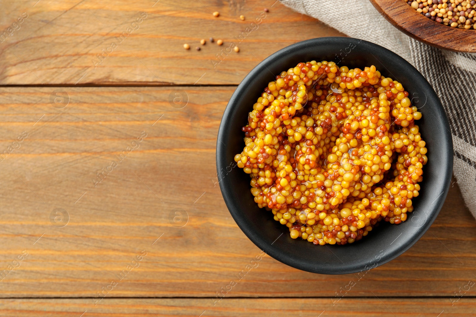 Photo of Fresh whole grain mustard in bowl on wooden table, top view. Space for text