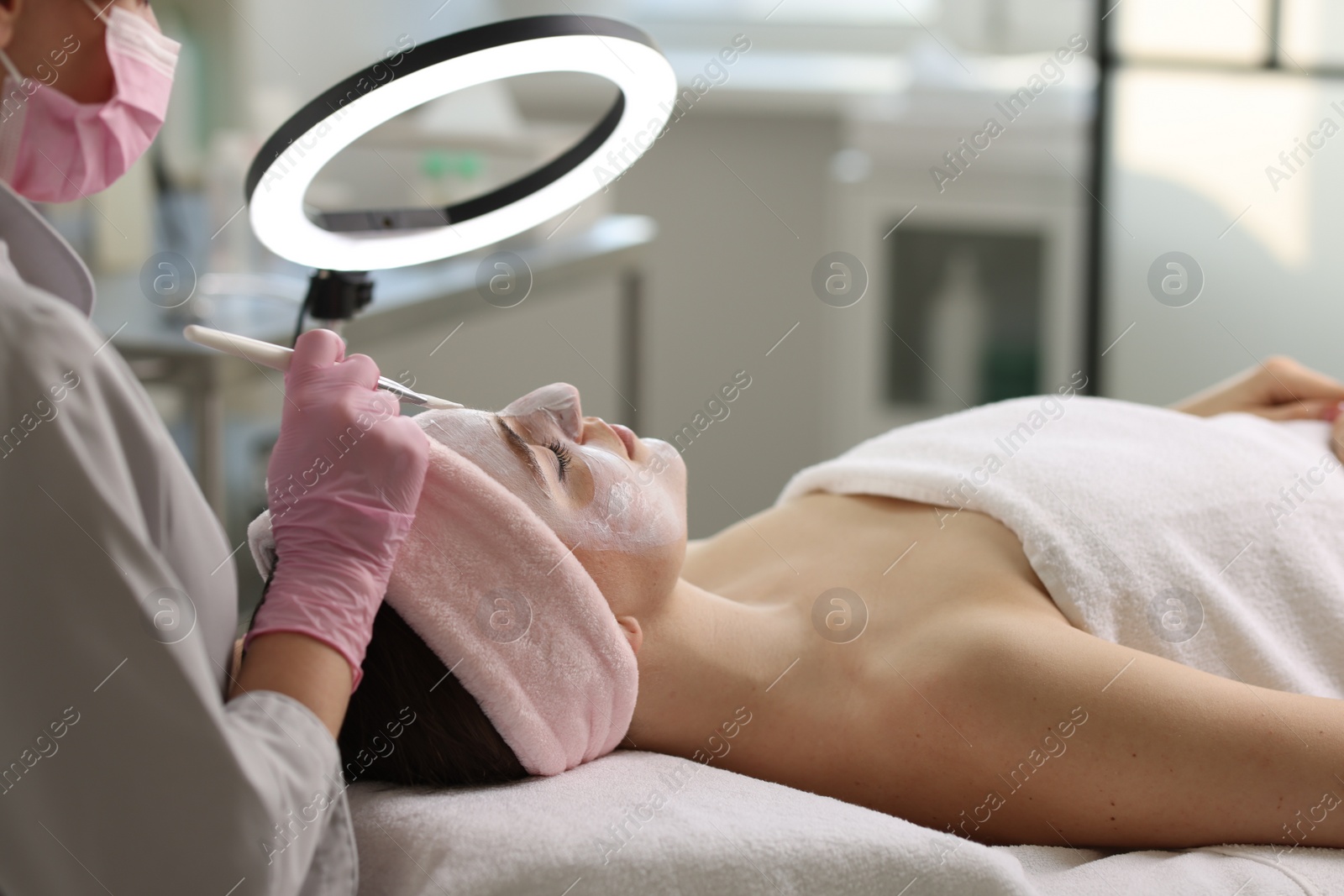 Photo of Cosmetologist applying mask on woman's face in clinic, closeup