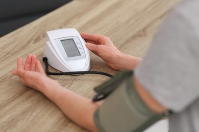 Woman checking blood pressure at wooden table indoors, closeup
