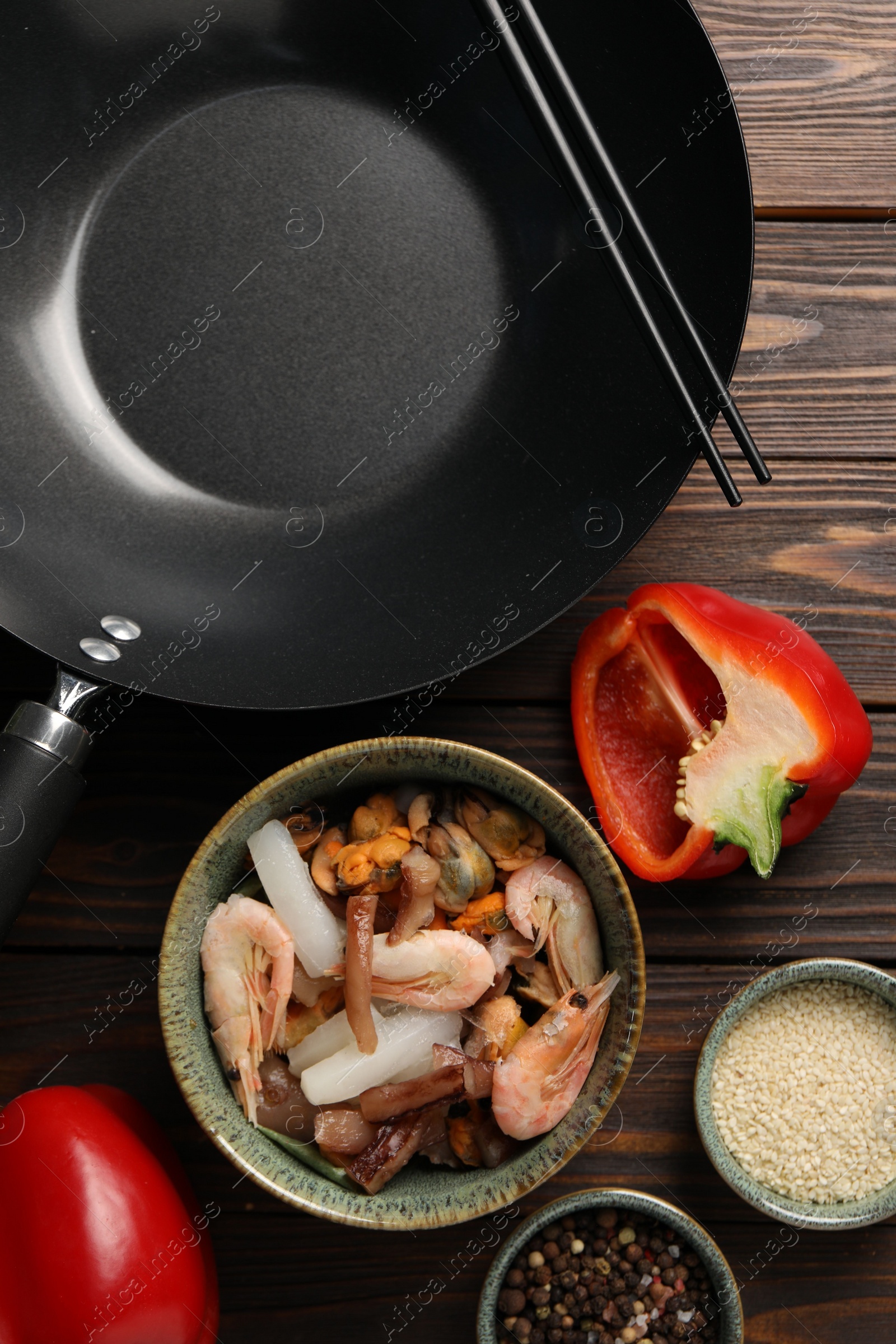 Photo of Black wok, chopsticks and products on wooden table, flat lay