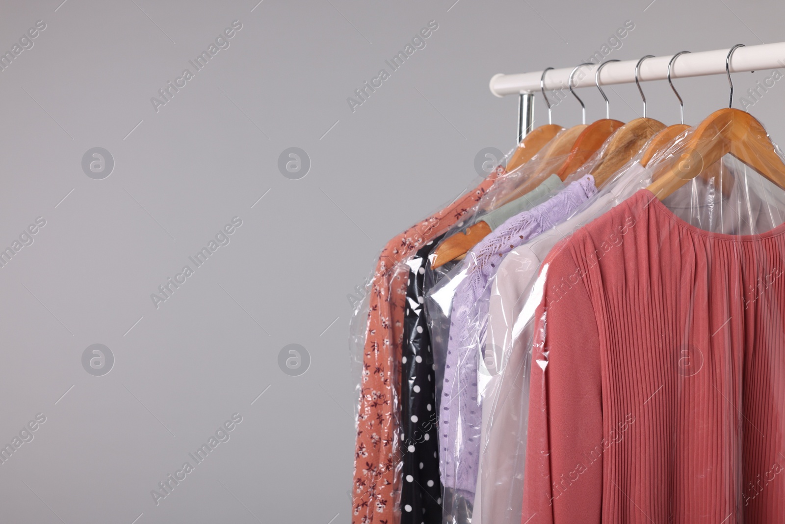 Photo of Dry-cleaning service. Many different clothes in plastic bags hanging on rack against grey background, space for text