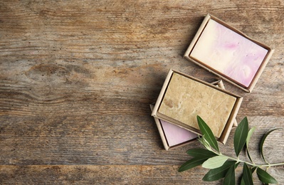 Photo of Packed handmade soap bars with olive twig and space for text on wooden table, top view