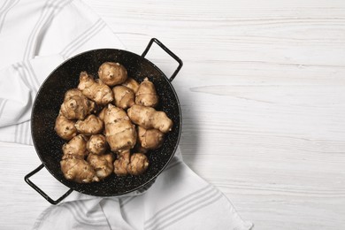 Photo of Pan with fresh Jerusalem artichokes on white wooden table, top view. Space for text