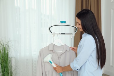 Woman steaming blouse on hanger at home. Space for text