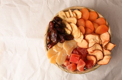 Photo of Wicker basket with different dried fruits on paper, top view. Space for text