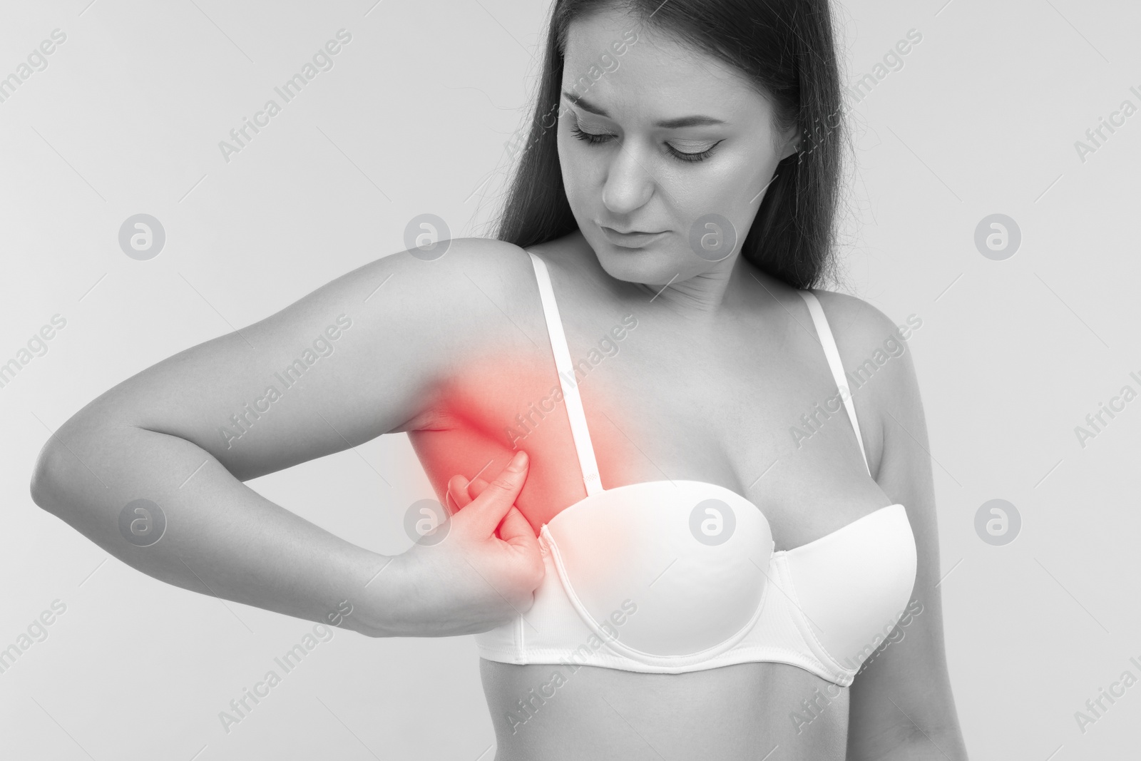 Image of Young woman suffering from breast pain on light grey background. Black and white with color accent effect