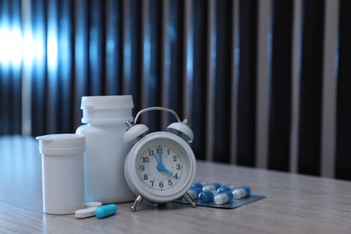 Photo of Alarm clock and pills on light wooden table, space for text. Insomnia treatment