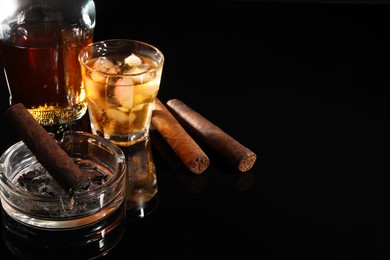 Photo of Smoldering cigar, ashtray and whiskey on black mirror surface. Space for text