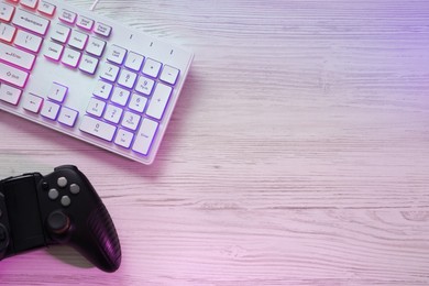 Photo of Modern RGB keyboard and game pad on white wooden table, flat lay. Space for text