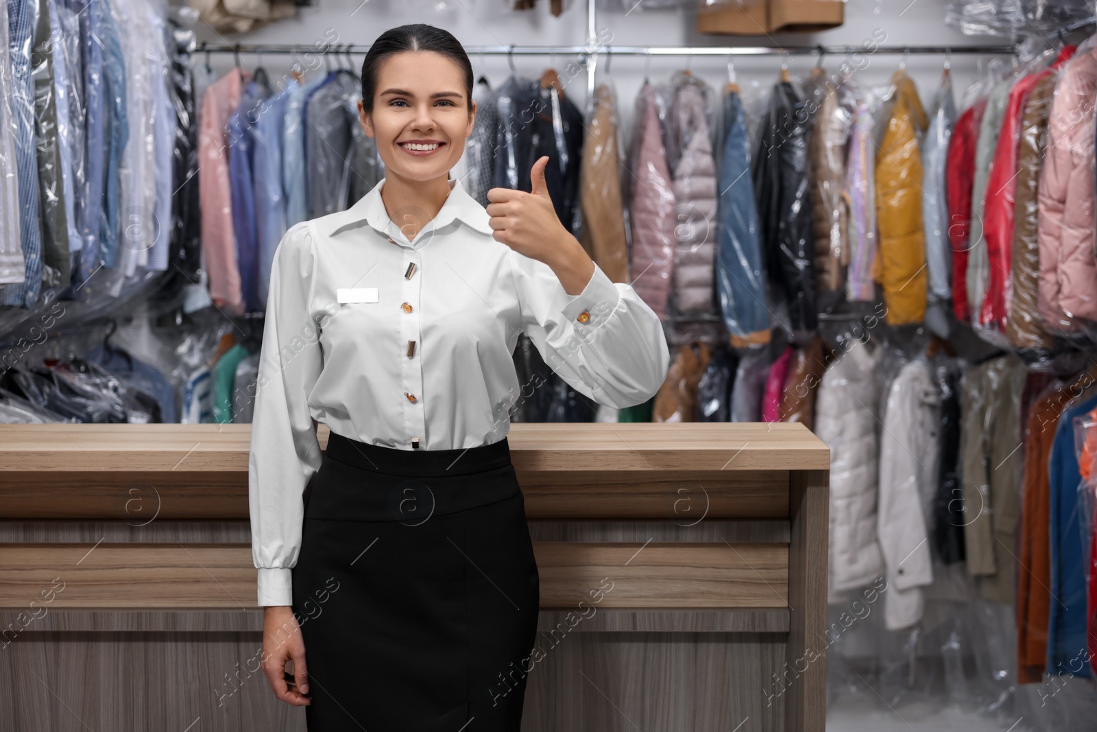 Photo of Dry-cleaning service. Happy worker showing thumb up near counter indoors, space for text