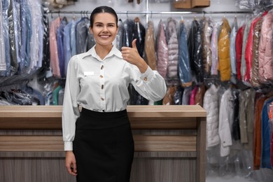 Dry-cleaning service. Happy worker showing thumb up near counter indoors, space for text