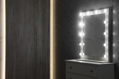 Modern mirror with light bulbs on grey chest of drawers in room. Space for text
