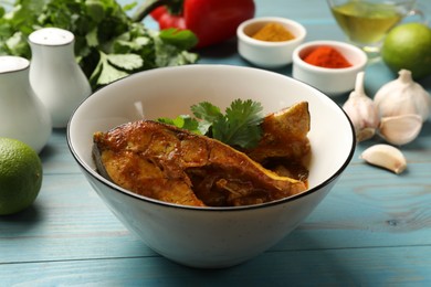 Photo of Tasty fish curry and ingredients on light blue wooden table, closeup. Indian cuisine