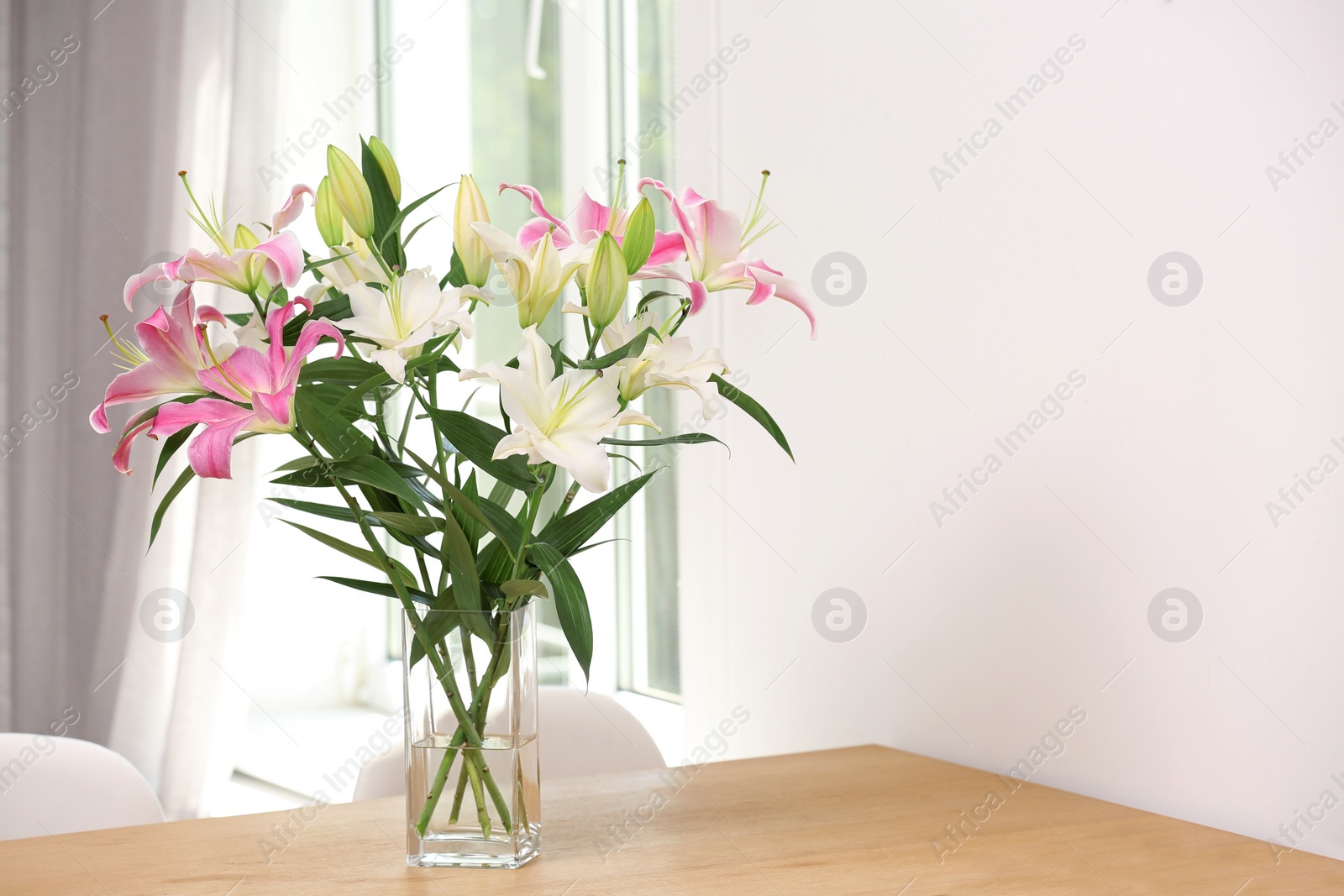 Photo of Vase with bouquet of beautiful lilies on wooden table indoors. Space for text