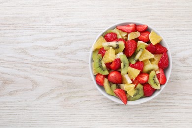 Photo of Delicious fresh fruit salad in bowl on white wooden table, top view. Space for text