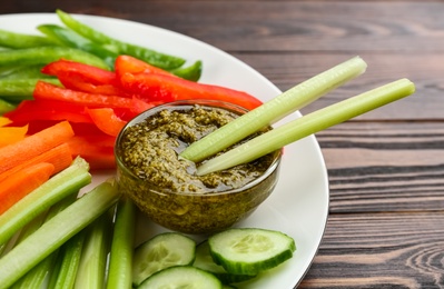 Photo of Celery and other vegetable sticks with dip sauce on wooden table, closeup