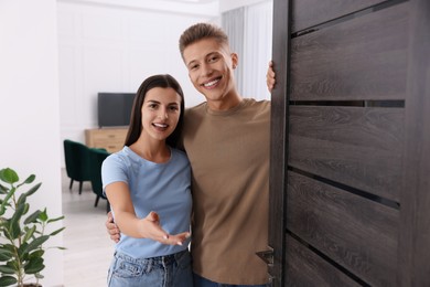 Photo of Happy couple welcoming near door. Invitation to come indoors