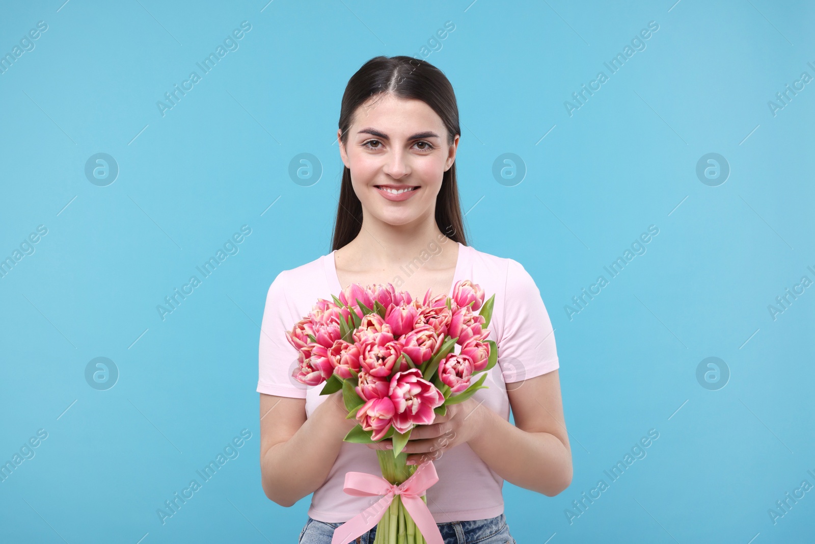 Photo of Happy young woman with beautiful bouquet on light blue background