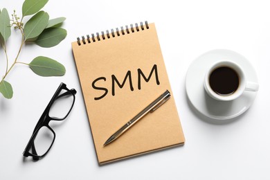 Image of Notebook with abbreviation SMM, cup of coffee and glasses on white background, flat lay. Social media marketing