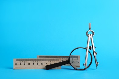 Photo of Rulers, magnifying glass and compass on light blue background