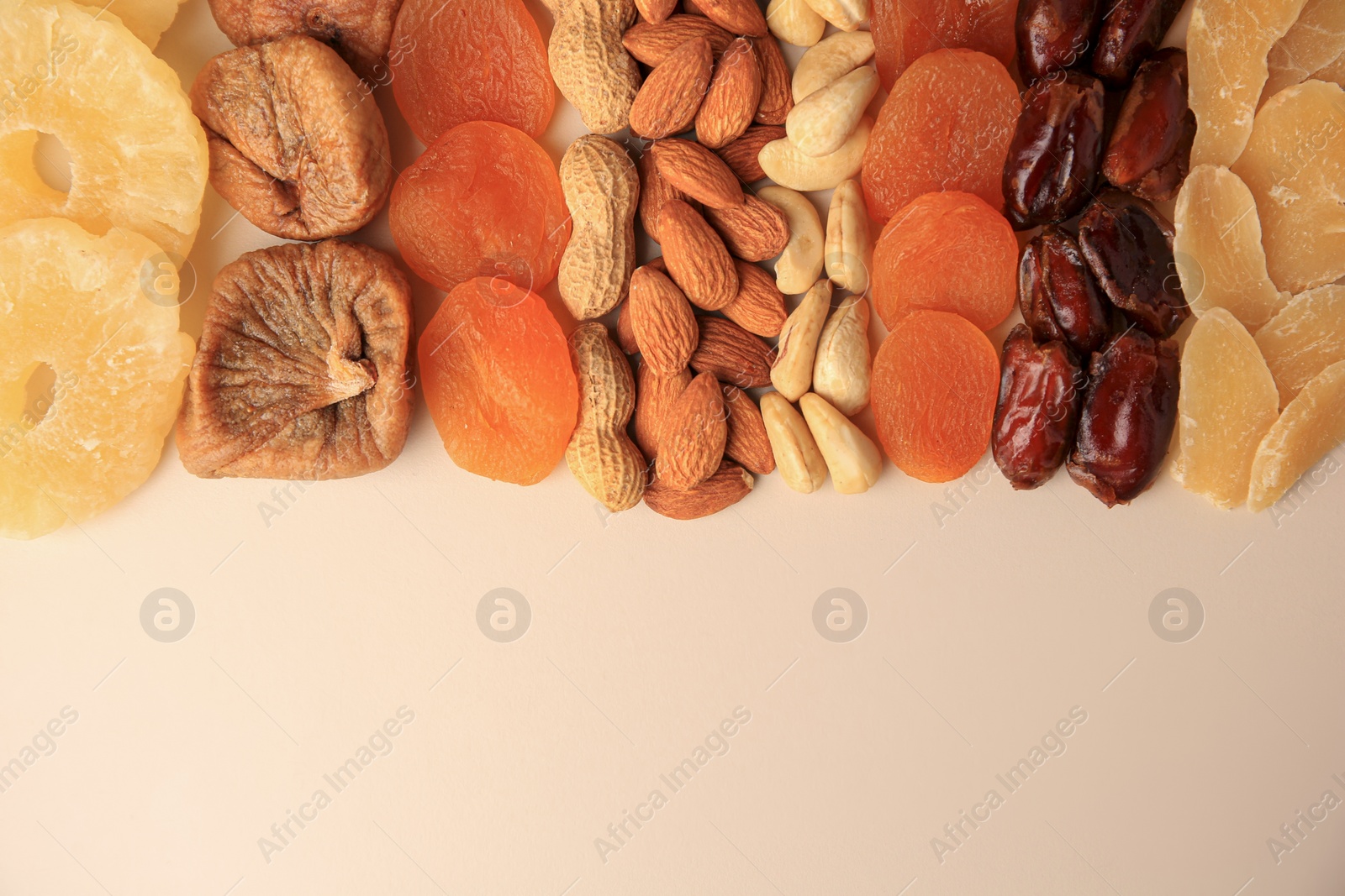 Photo of Different tasty nuts and dried fruits on beige background, flat lay. Space for text