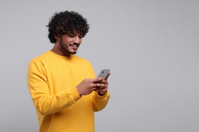 Photo of Handsome smiling man using smartphone on light grey background, space for text