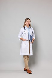 Portrait of happy doctor with stethoscope and clipboard on light grey background