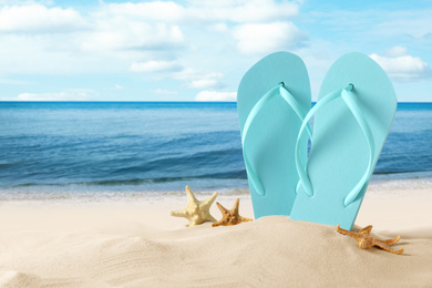 Image of Beach slippers and starfishes on sandy beach near sea. Summer vacation