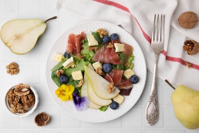 Tasty salad with brie cheese, prosciutto, walnuts and pear served on white tiled table, flat lay